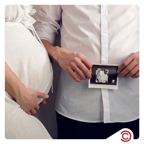 Cuplu de viitori părinți ținându-se de mână pe burtica soției, în natură